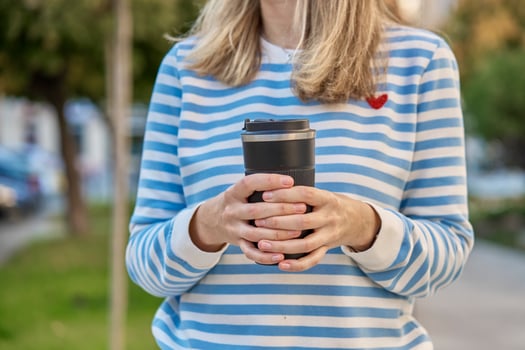Woman holding black reusable coffee cup outdoors. Concept of eco-friendly lifestyle photo