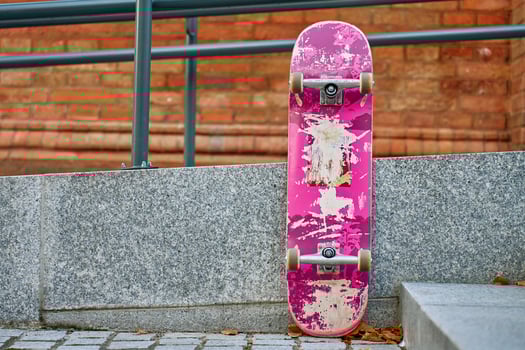 Used scratched pink skateboard against stone wall at city street. Urban sport and youth subculture concept photo