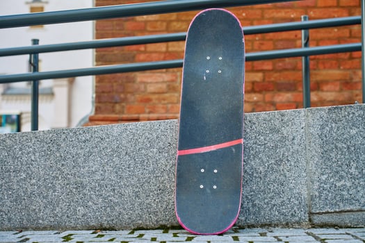 Used scratched pink skateboard against stone wall at city street. Urban sport and youth subculture concept photo