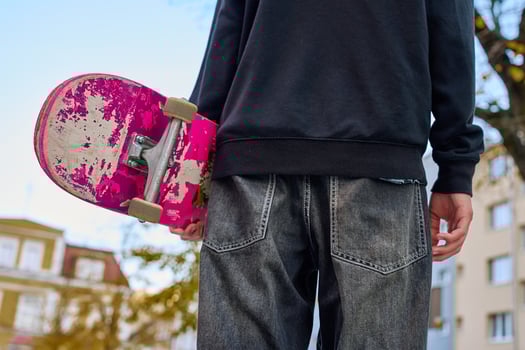 Skateboarder in baggy jeans holding scratched skateboard walking at city street. Teenager is skateboarding. Concept of youth subculture photo