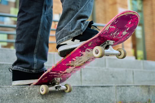 Skateboarder balancing on pink skateboard. Close-up of teenager feet wearing jeans and black sneakers skateboarding at street stairs. Leisure activity and extreme sport concept photo