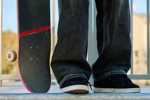 Skateboarder in baggy jeans holding scratched pink skateboard at city street. Teenager is skateboarding. Concept of youth subculture photo