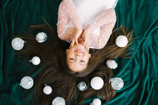 A cute smiling girl with long hair is lying on her back on a green blanket. On her hair are white Christmas balls. Happy Christmas and New Year concept. photo