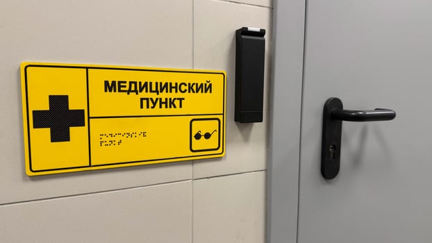 Entrance to medical center at station to assist passengers, sign with medical sign and braille text to indicate place of first aid in public place. Inscription in Russian - medical station photo