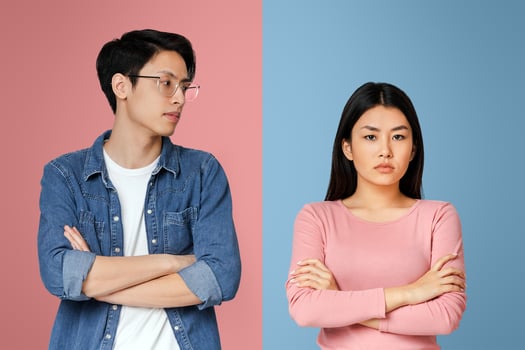 Asian young man looking with sorrow at his angry girlfriend, couple fight over grey background photo