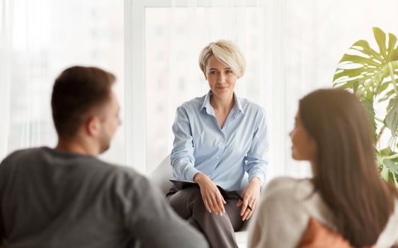 Happy Family Psychologist Smiling Looking At Couple's Reconciliation During Therapy Session Sitting In Office. Selective Focus photo