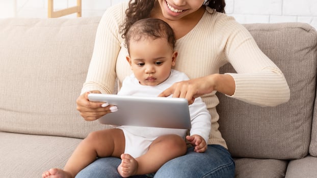 Smiling African Mommy Holding Baby Son Using Digital Tablet Showing Toddler Educational Game On Computer Spending Time Learning And Having Fun Online Sitting On Sofa At Home. Family Gadget, Technology photo