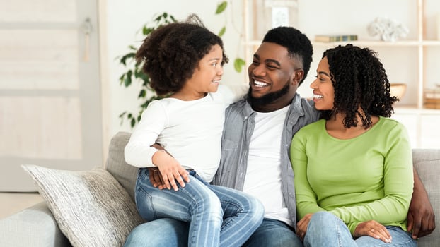 Family Time. Happy African American Parents Bonding With Their Little Daughter At Home, Sitting On Couch In Living Room Together And Smiling photo