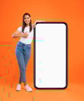 Mobile Offer. Happy woman leaning on huge cellphone with blank white screen, showing thumb up gesture, recommending great new app or website for phone, offering space for ad, mock up, full body length photo