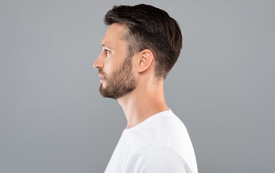 Profile portrait of middle-aged bearded man in white t-shirt over grey studio background, copy space. Side view of handsome confident man posing on gray, standing straight and looking aside photo