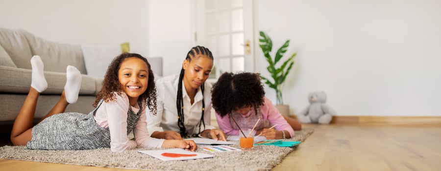 Two black cheerful children lie on a soft rug while creating colorful drawings with an adult nearby. The warm atmosphere is filled with creativity and laughter as they enjoy their time together. photo