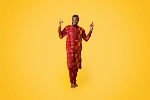 Cheerful black man in african costume gesturing over yellow background, pointing up photo