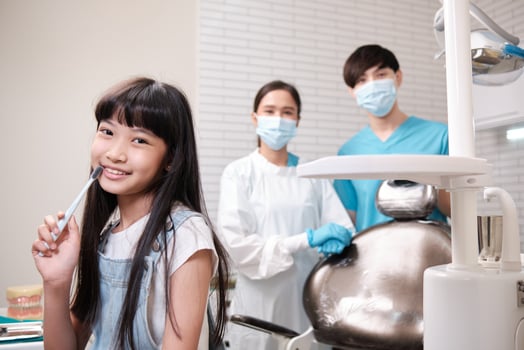Portrait of Asian female pediatric dentist, assistant, and a girl patient smiling and looking at camera in dental clinic, mouth hygiene, and professional orthodontic healthcare work in a kid hospital. photo