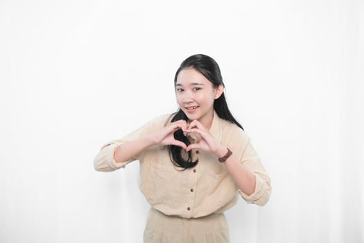 The expression of an Indonesian Asian model woman in white is smiling and making a love code photo