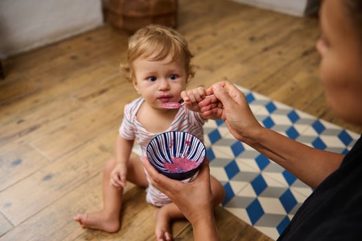 Mother feeding her baby with spoon in kitchen setting photo