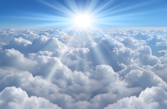 Bright sun shining through fluffy white clouds in blue sky photo