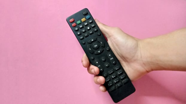 Close up of a hand holding a black TV remote control against a pink background. Concept of technology, entertainment, and media. photo