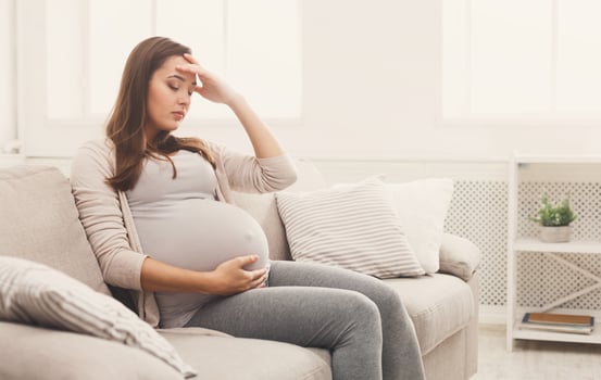 Young pregnant woman with headache sitting on sofa. Pregnancy symptoms, expectation, parenthood concept, copy space photo