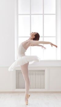 Classical Ballet dancer side view. Beautiful graceful ballerine practice ballet positions in tutu skirt near large window in white light hall. Ballet class training, high-key soft toning. photo