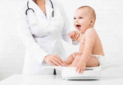 Weight measuring. Adorable little baby sitting on scales , medical check up with female pediatrician, copy space photo