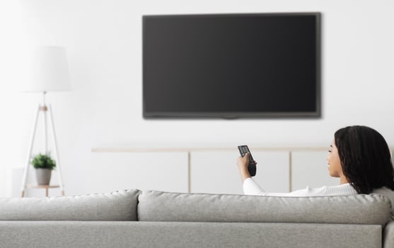 African american woman watching TV pointing remote control at flatscreen plasma television set with blank screen, switching channels while sitting on sofa at home, mockup photo