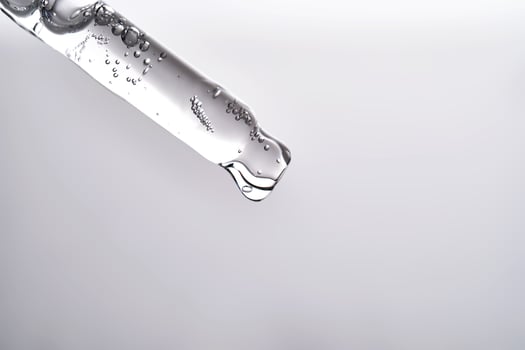 Pipette with facial serum pouring out of it on grey background. photo