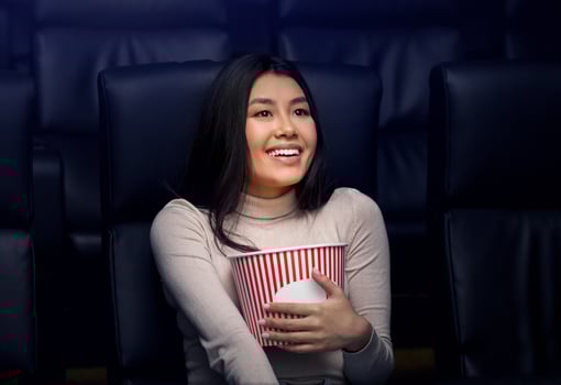 Going to movies alone concept. Lovely Asian woman with popcorn enjoying film in cinema photo