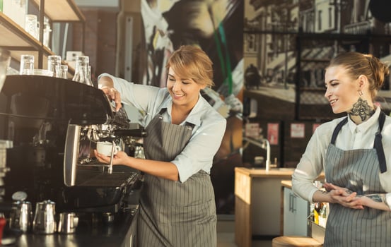Skilled barista teaching young tattooed girl to brew coffee in professional coffee machine. Sharing secrets of restaurant business. Small business and experience exchange concept photo