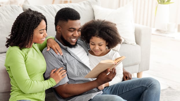 Family Leisure. Black Man Reading Book With His Wife And Daughter At Home, Relaxing Together On Floor In Living Room photo