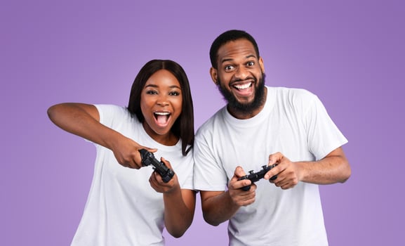 Having Fun. Portrait of excited African American couple playing games together with a black controller, holding and using joysticks over blue studio background, banner. Free Time Entertainment photo