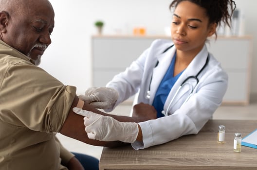 Close up of black female doctor in protective gloves applying sticking patch to patient's arm after injecting elderly man with seasonal flu or infection vaccine, selective focus on hand photo