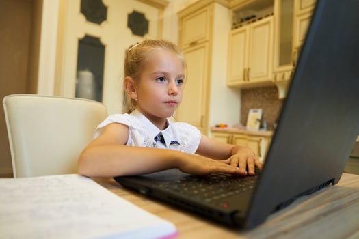 Young girl focused on her laptop while studying at a kitchen table photo
