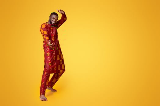 Funny handsome guy in african dress dancing and posing over yellow background photo