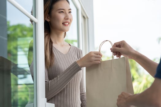 Happy smiling Asian woman receives paper bag parcel of food from courier front house. Delivery man send deliver express. online shopping, paper container, takeaway, postman, delivery service, packages photo