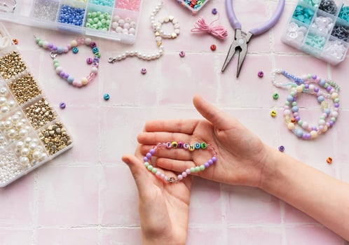 Child making beaded bracelets at home on pink tiled table photo
