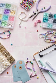 Colorful beads and jewelry making supplies arranged on pink tile background with clipboard and pens photo