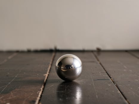 A small silver ball sits on a wooden floor. photo