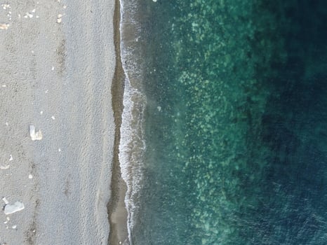 Aerial view from above on calm azure sea and pebbles beach. Small waves on cristal clear water surface in motion blur. Summer ocean sea beach background. Nobody. Holiday, vacation and travel concept photo