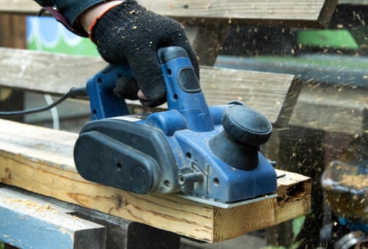 A man works with an electric tool with an electric planer, cleans old wood. Industry, close-up photo