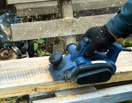 A man works with an electric tool with an electric planer, cleans old wood. Industry, close-up photo