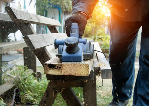 A man works with an electric tool with an electric planer, cleans old wood. Industry, sunset photo