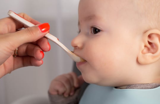Mother feeds baby boy vegetable puree from a spoon. Feeding children 7 months. Close-up photo