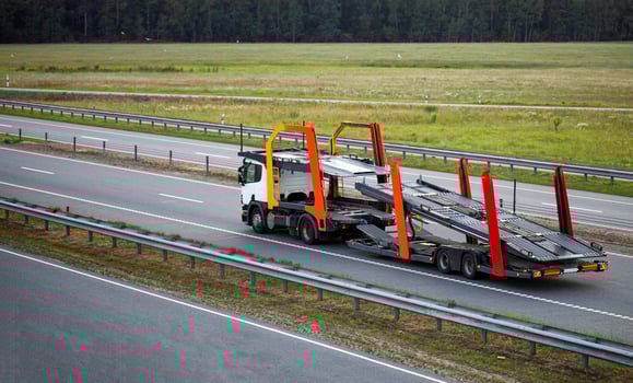 An empty tractor-trailer truck with a semi-trailer car transporter drives along the highway in the summer against the backdrop of sunset behind new cars. Concept for transporting cars photo