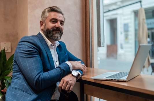 Portrait of a happy mature business man sitting at his desk in the office or restaurant cafe near the window while working on a laptop. photo