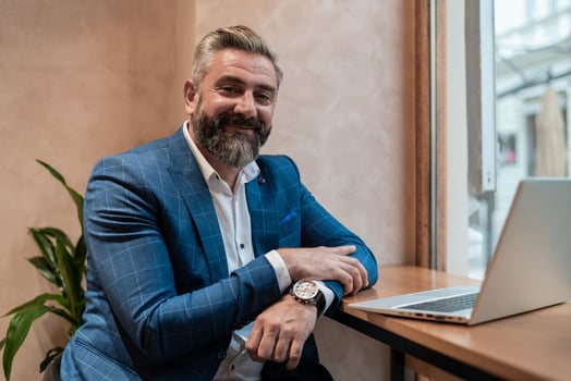 Portrait of a happy old business man sitting at his desk in the office or restaurant cafe near the window and working on a laptop. photo