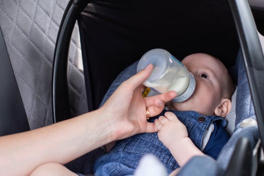 mother feeds the baby in, car seat in the car, milk from a bottle. Feeding children in car seats, close-up photo