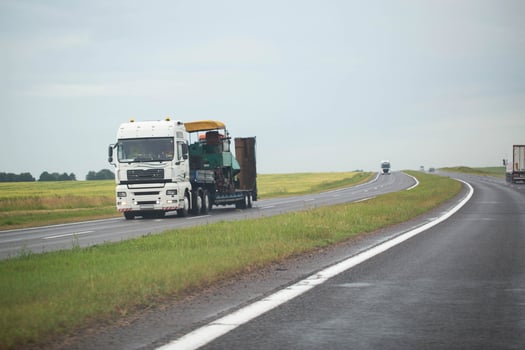 White semi-trailer truck trawl transports oversized machinery on the highway in rainy weather, industry. Copy space for text photo