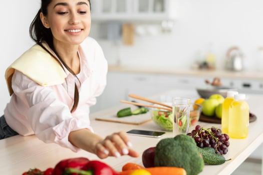 Portrait Of Smiling Millennial Woman Cooking Healthy Vegetarian Food Standing In Kitchen, Slim Fit Lady Preparing Vegetable Salad For Lunch At Home, Reaching For Carrot, Free Copy Space photo