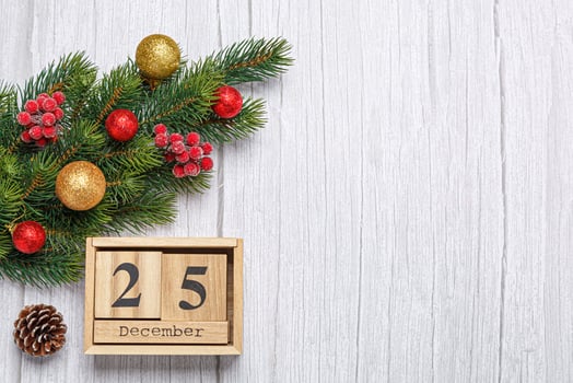 christmas tree branch with toys and gifts and wooden calendar december 25 on wooden background photo