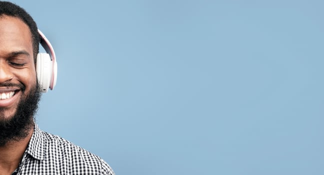 Perfect Song. Closeup portrait of smiling african guy listening to music or podcast in headset isolated on blue studio wall photo